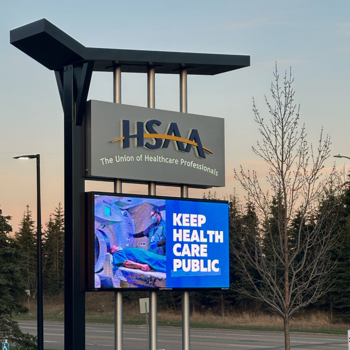 A sign outside the HSAA office with the logo and a digital screen that says "Keep Health Care Public"